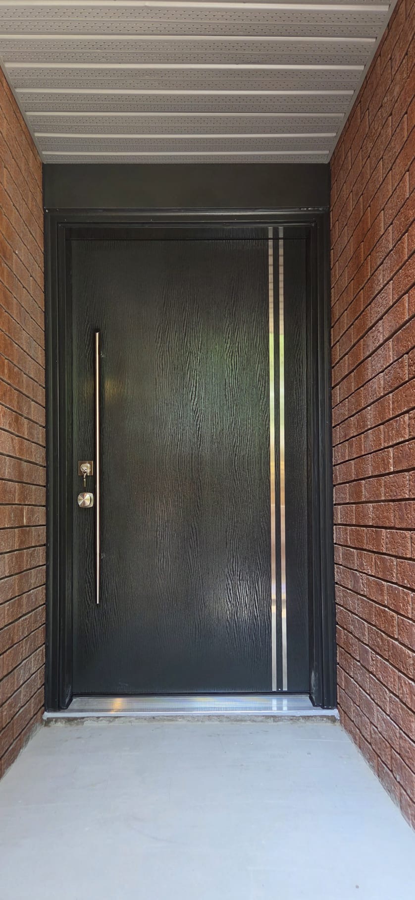 Brick porch entry after installing a black woodgrain entry door with stainless pull and privacy glass strip